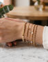 Detalle de la muñeca de una mujer luciendo una combinación de varias pulseras y brazaletes de oro finos de la marca Virguliilla.