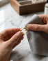 Manos frotando suavemente un anillo de la marca Virguliilla con un paño de microfibra específico para limpiar joyas sobre una superficie de mármol.